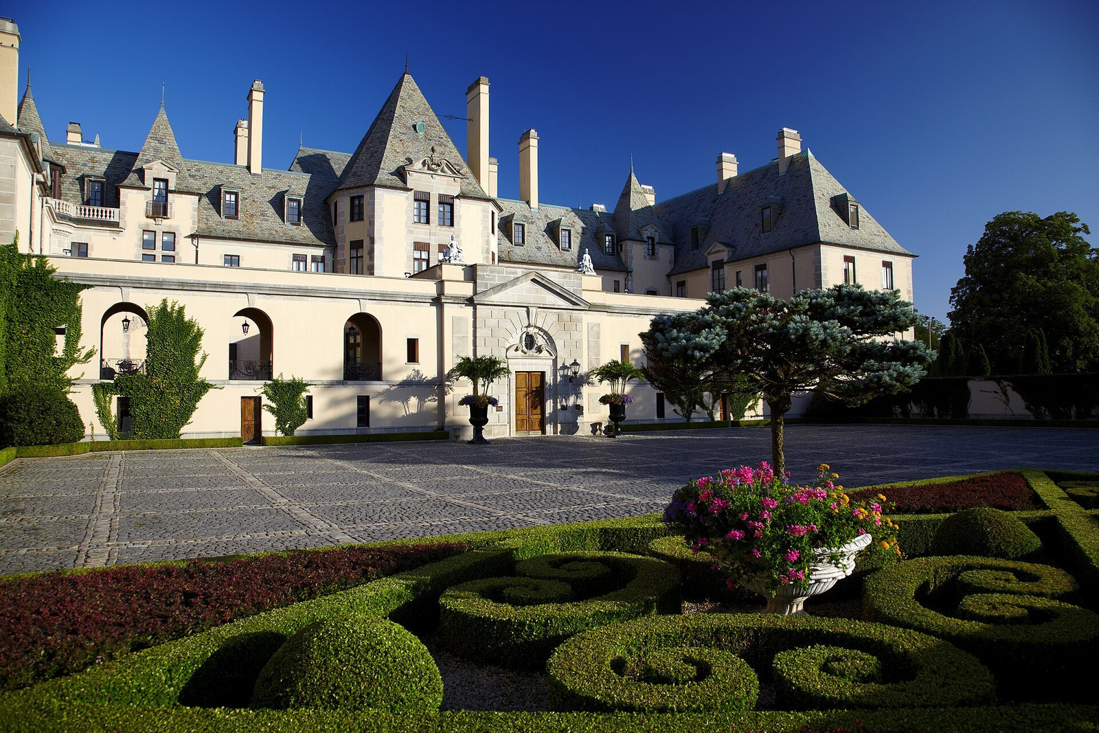Formal courtyard at Oheka Castle with clipped hedges, patterned beds, and the main entrance