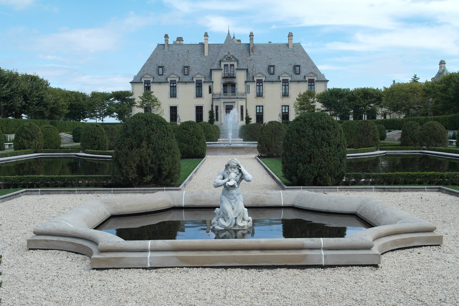 Fountain, sculpture, reflecting pools, and clipped shrubs aligned with Oheka Castle