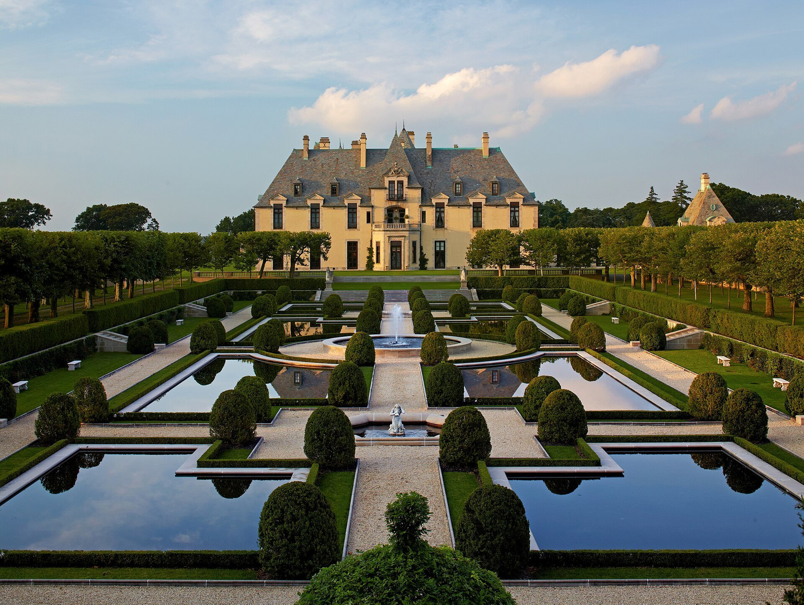 Oheka Castle centered beyond geometric reflecting pools and clipped formal gardens