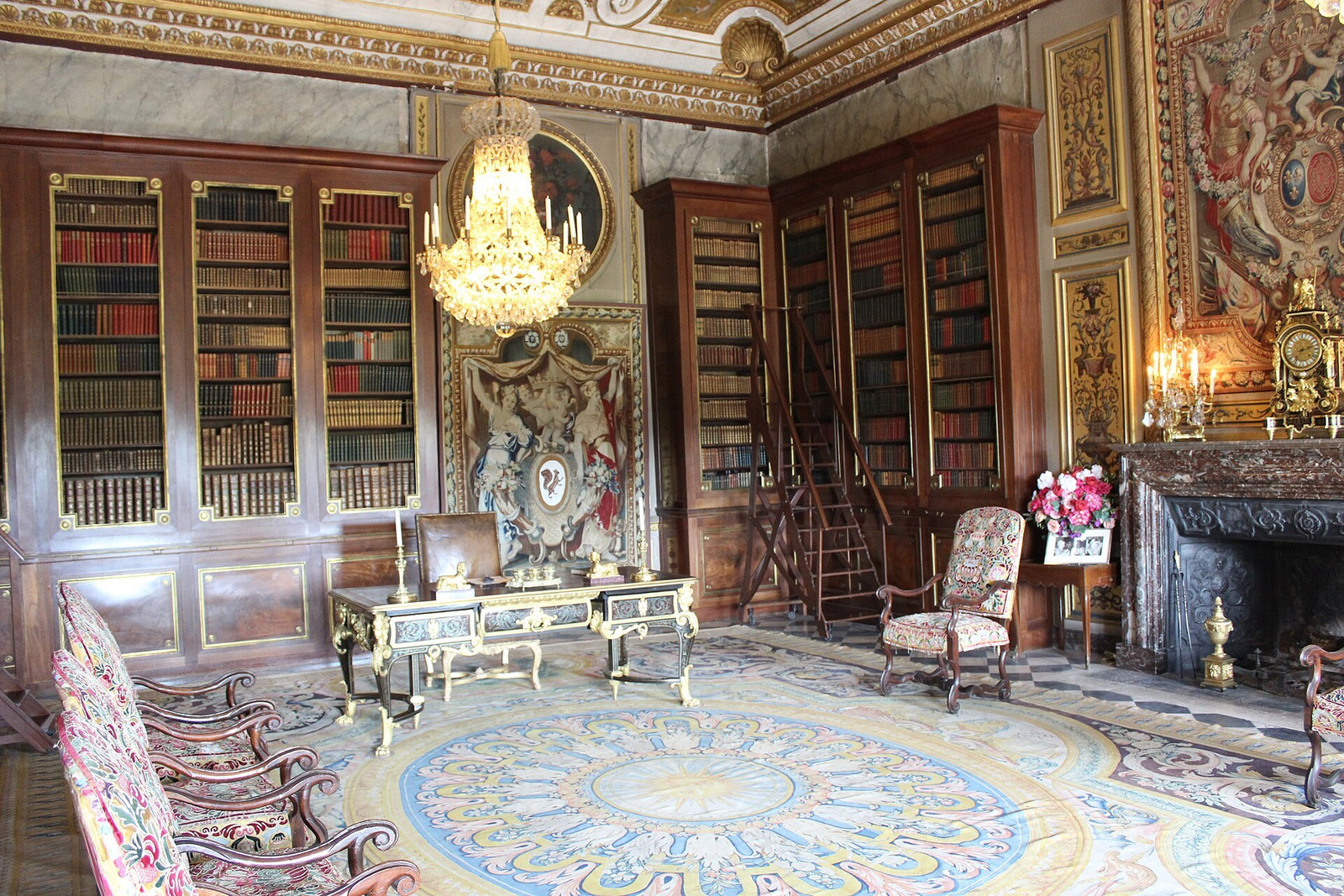 A principal interior at Vaux-le-Vicomte with bookcases, tapestry, fireplace, and chandelier